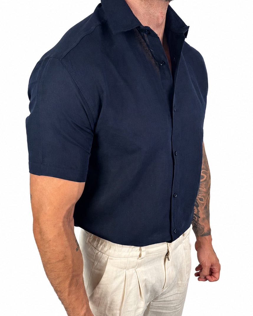A muscular man wearing a navy blue short-sleeve button-down shirt and off-white linen trousers, shown from the waist down against a plain white background.