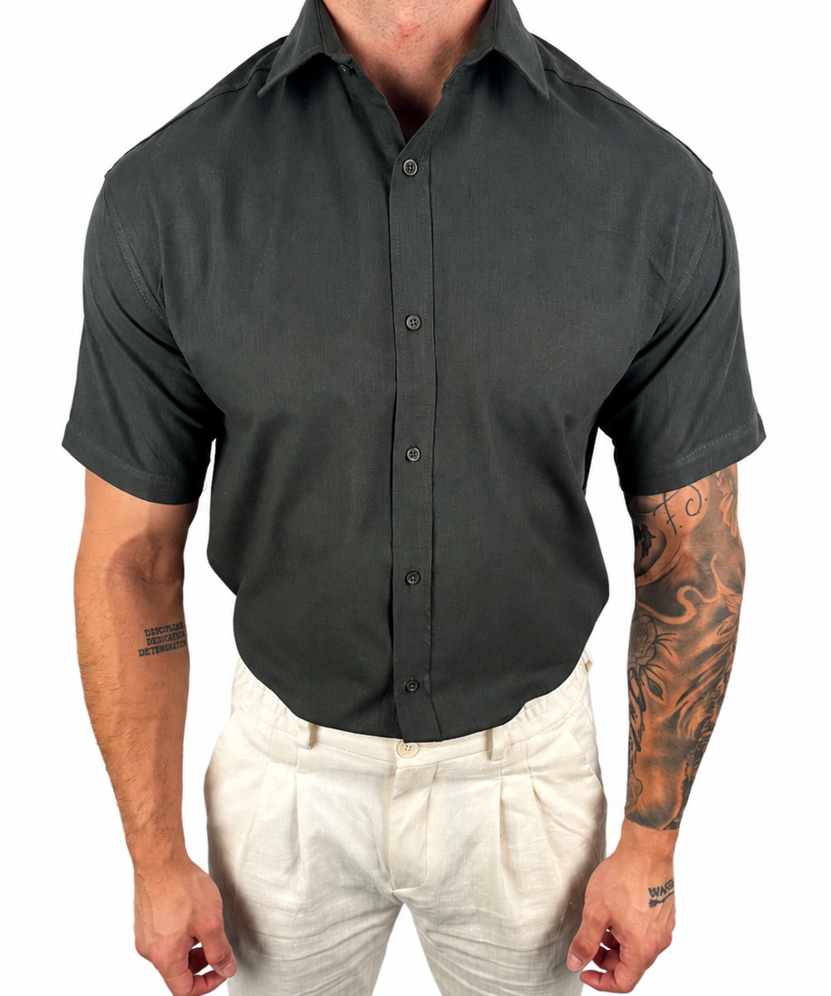 A man wearing a dark charcoal gray short-sleeve button-down shirt tucked into light beige linen trousers, shown from the neck down against a plain white background.