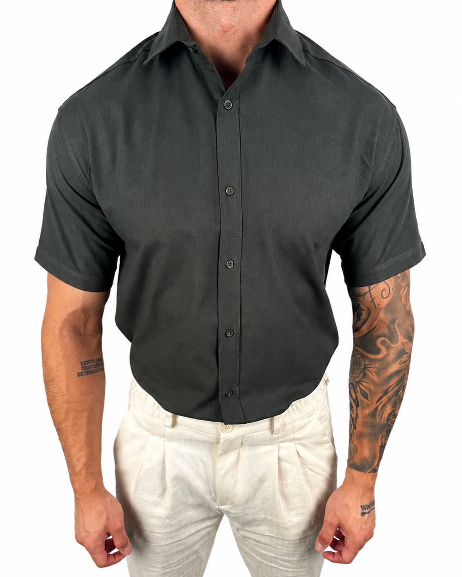 A man wearing a dark charcoal gray short-sleeve button-down shirt tucked into light beige linen trousers, shown from the neck down against a plain white background.
