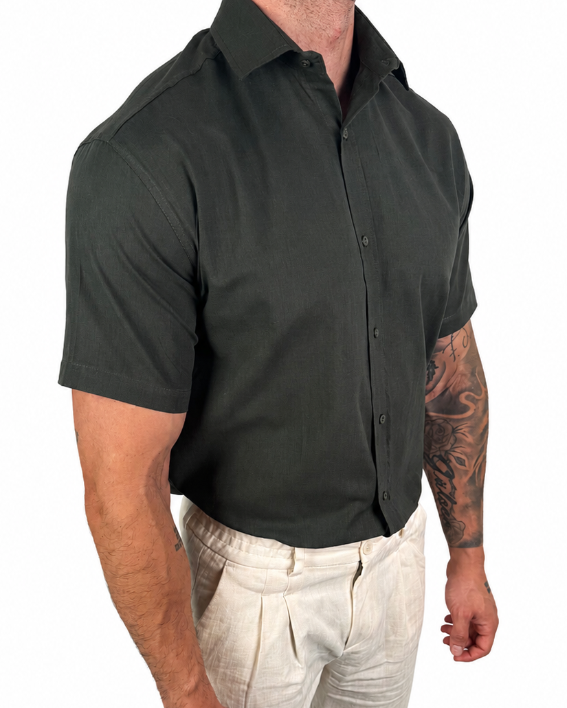 A man wearing a dark charcoal gray short-sleeve button-down shirt and light beige linen trousers, shown from the waist down against a plain white background.