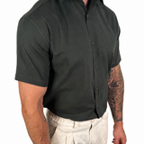 A man wearing a dark charcoal gray short-sleeve button-down shirt and light beige linen trousers, shown from the waist down against a plain white background.
