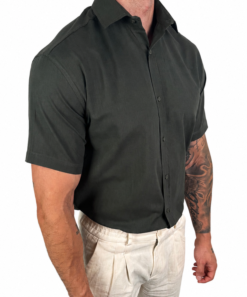 A man wearing a dark charcoal gray short-sleeve button-down shirt and light beige linen trousers, shown from the waist down against a plain white background.