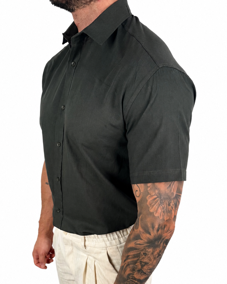 A man wearing a dark charcoal gray short-sleeve button-down shirt and off-white trousers, shown from a side profile against a plain white background.