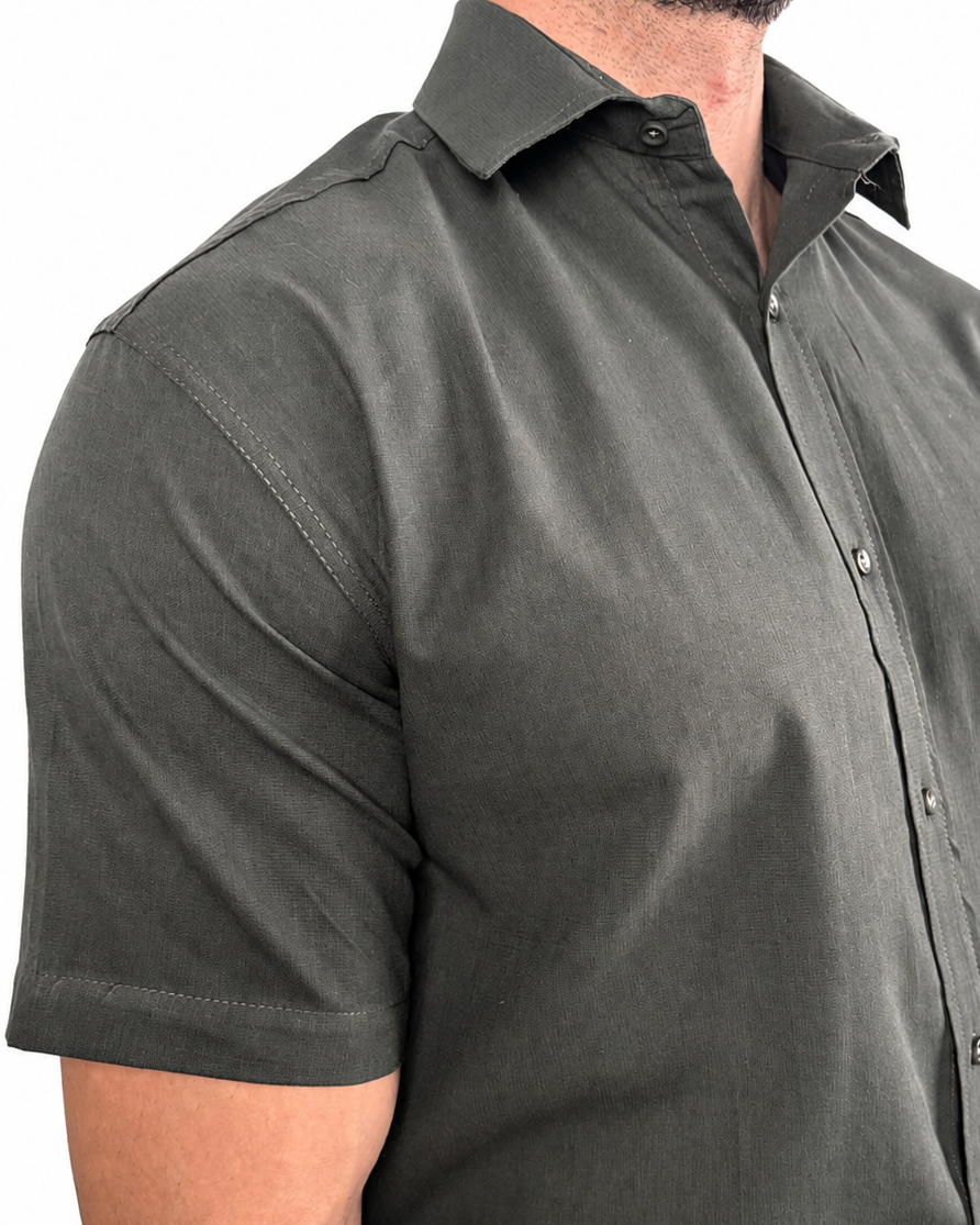 A man wearing a dark olive green short-sleeve button-down shirt, cropped from the neck down, against a plain white background.