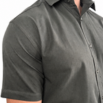 A man wearing a dark olive green short-sleeve button-down shirt, cropped from the neck down, against a plain white background.