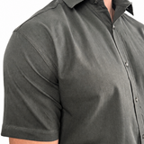 A man wearing a dark olive green short-sleeve button-down shirt, cropped from the neck down, against a plain white background.