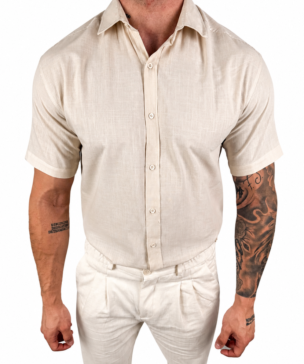 A man wearing a light beige short-sleeve linen button-up shirt and matching beige trousers, shown from the neck down against a plain white background.