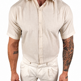 A man wearing a light beige short-sleeve linen button-up shirt and matching beige trousers, shown from the neck down against a plain white background.