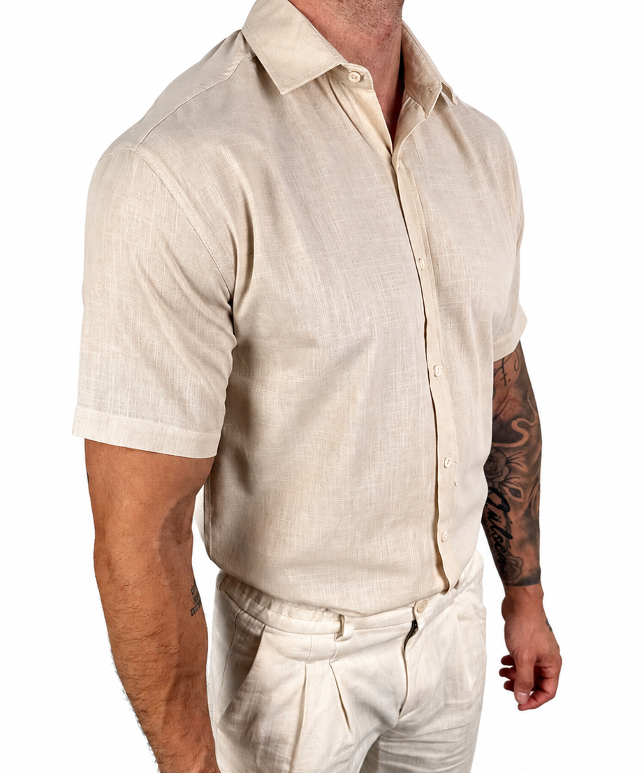 A man wearing a light beige short-sleeve linen button-up shirt and matching beige trousers, shown from the chest down against a plain white background.
