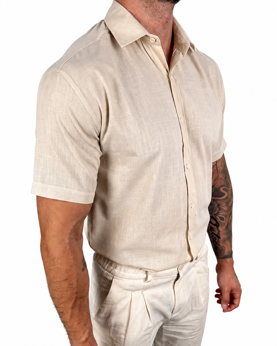 A man wearing a light beige short-sleeve linen button-up shirt and matching beige trousers, shown from the chest down against a plain white background.