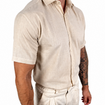 A man wearing a light beige short-sleeve linen button-up shirt and matching beige trousers, shown from the chest down against a plain white background.