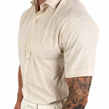 A man wearing a light beige linen short-sleeve button-up shirt and matching linen trousers, shown from the side against a plain white background.