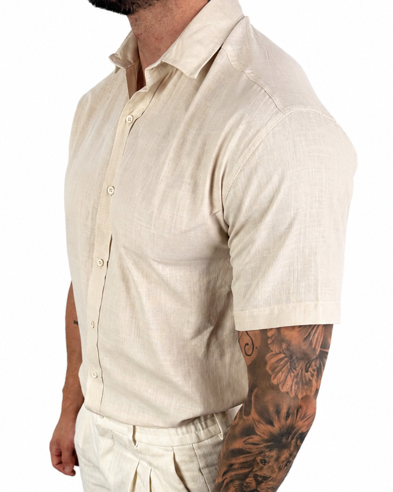 A man wearing a light beige linen short-sleeve button-up shirt and matching linen trousers, shown from the side against a plain white background.