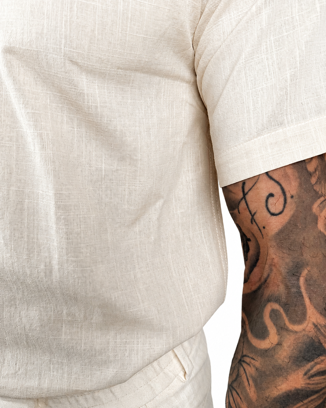 Close-up of a person wearing a short-sleeve cream-colored linen shirt, showing the textured fabric and a tattooed arm.