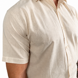 A close-up of a man wearing a short-sleeve linen button-down shirt in a light cream or beige color, showing the texture of the fabric.