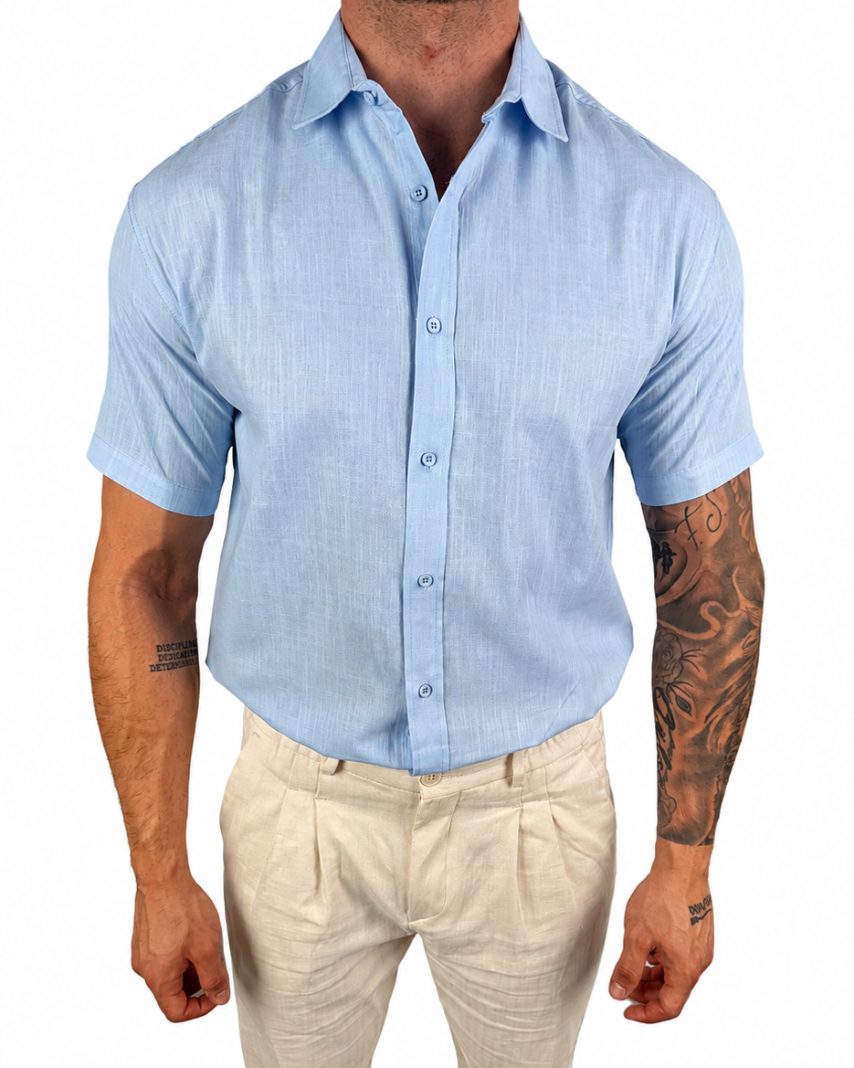 A man wearing a light blue short-sleeve button-up shirt and beige trousers, shown from the neck down against a plain white background.