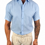 A man wearing a light blue short-sleeve button-up shirt and beige trousers, shown from the neck down against a plain white background.