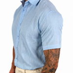 A man wearing a light blue short-sleeve button-down shirt and beige trousers, shown from the waist down in a side profile against a white background.