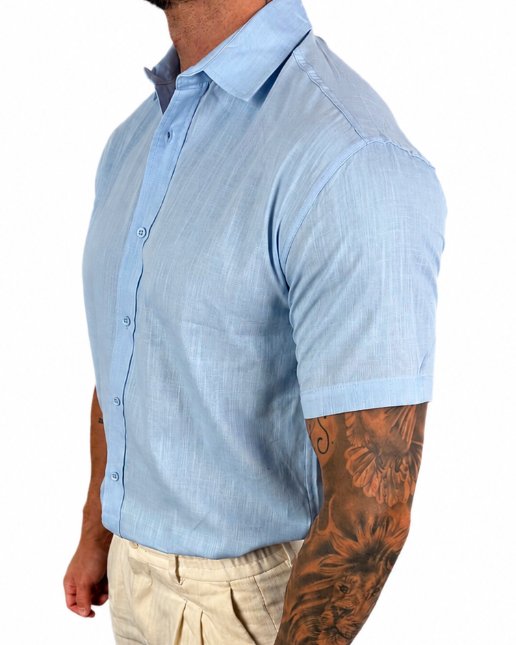 A man wearing a light blue short-sleeve button-down shirt and beige trousers, shown from the waist down in a side profile against a white background.