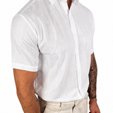 A man wearing a white short-sleeve linen button-down shirt and beige trousers, shown from the neck down against a plain white background.
