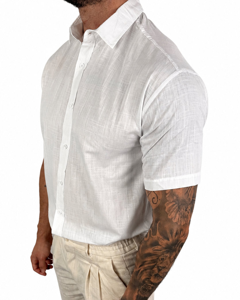 A muscular man wearing a white short-sleeve linen button-down shirt and beige trousers, shown from the waist up against a plain white background.