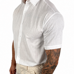 A muscular man wearing a white short-sleeve linen button-down shirt and beige trousers, shown from the waist up against a plain white background.