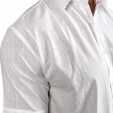 A close-up of a man wearing a white short-sleeve linen button-down shirt, showing the textured fabric and collar.