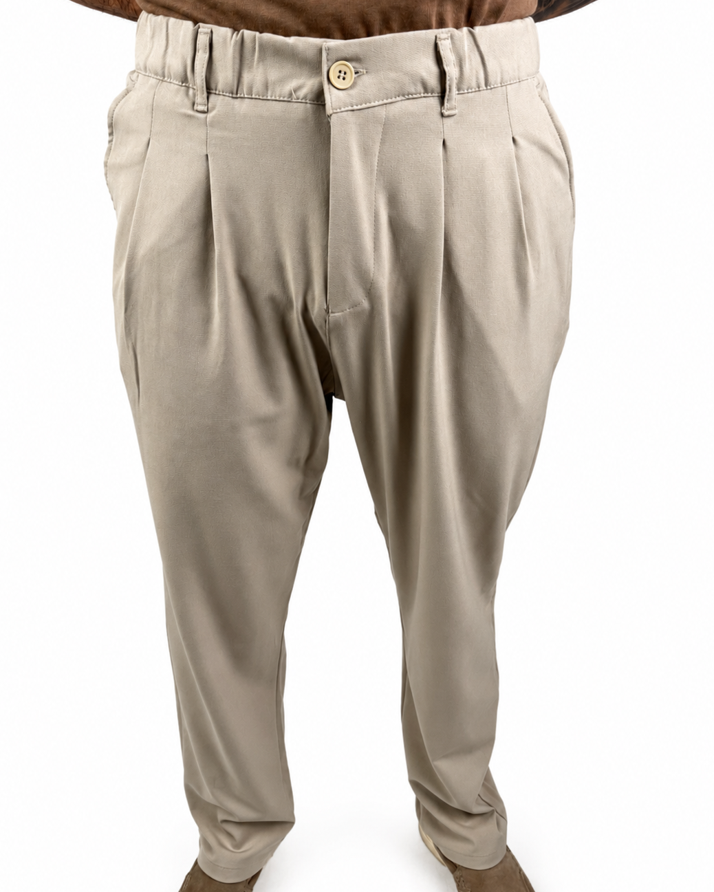 A pair of men's beige pleated trousers shown on a model from the waist down, paired with brown shoes and a brown shirt against a white background.