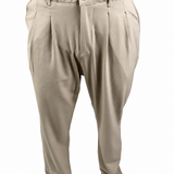 A pair of men's beige pleated trousers shown on a model from the waist down, paired with brown shoes and a brown shirt against a white background.