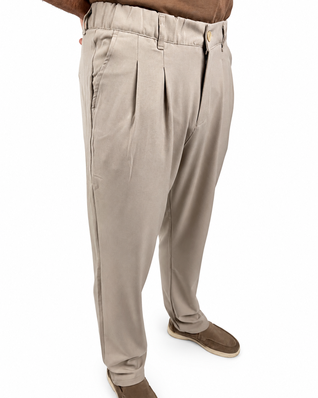 A person wearing light beige pleated trousers and brown slip-on shoes, shown from the waist down against a plain white background.