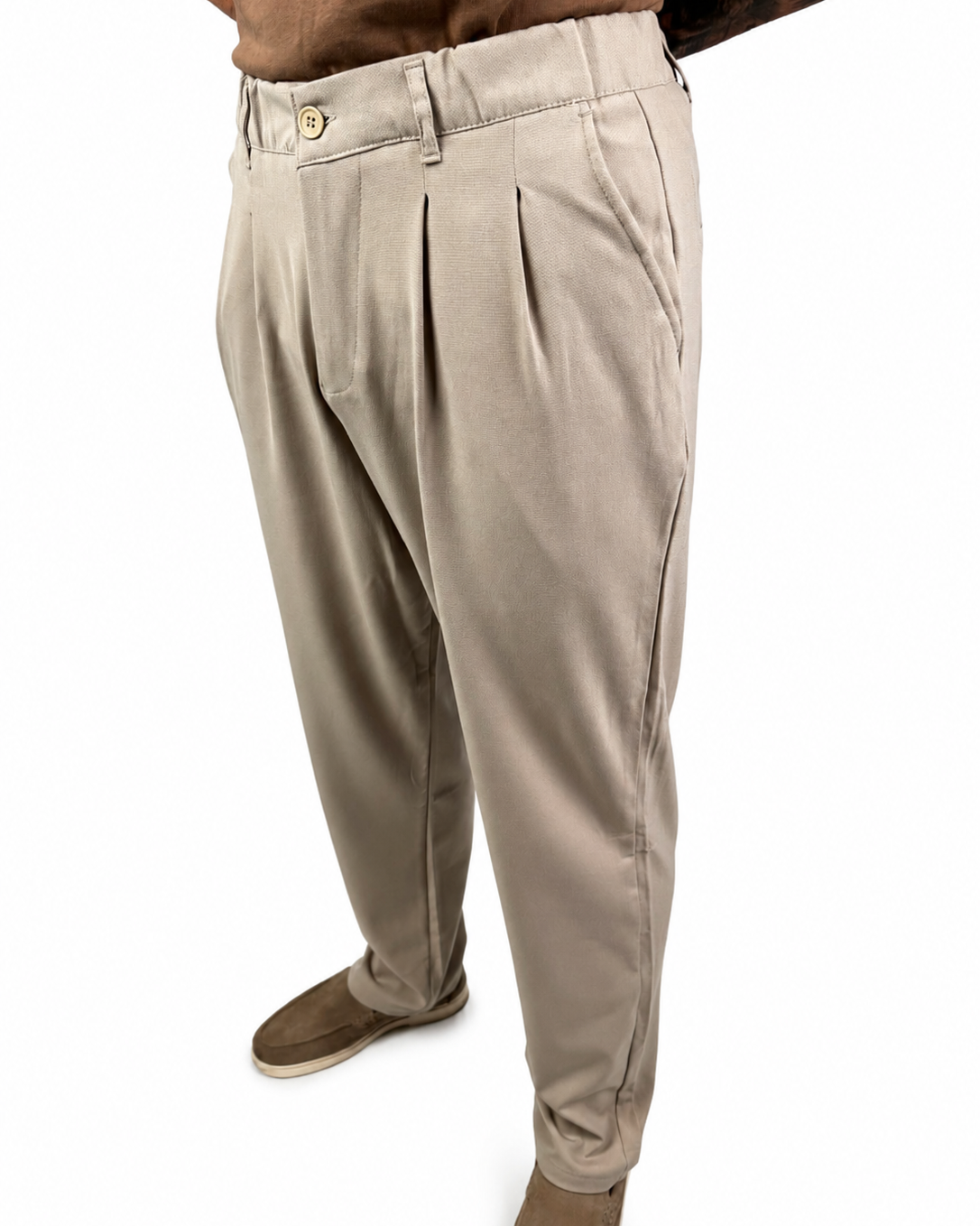 A person wearing light beige pleated trousers with brown shoes, shown from the waist down against a plain white background.