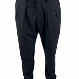 Black pleated trousers shown on a model from the waist down, paired with tan suede shoes against a plain white background.