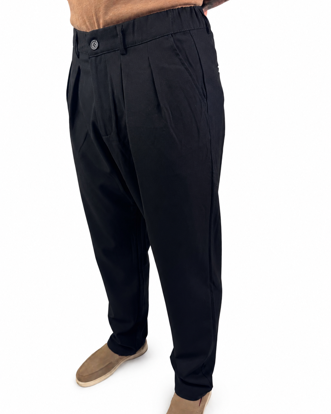 A person wearing black pleated trousers with tan suede shoes, shown from the waist down against a plain white background.