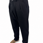 A person wearing black pleated trousers with tan suede shoes, shown from the waist down against a plain white background.