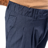 Close-up of a person wearing navy blue pleated trousers and a tan t-shirt, focusing on the waistband and side pocket details against a white background.