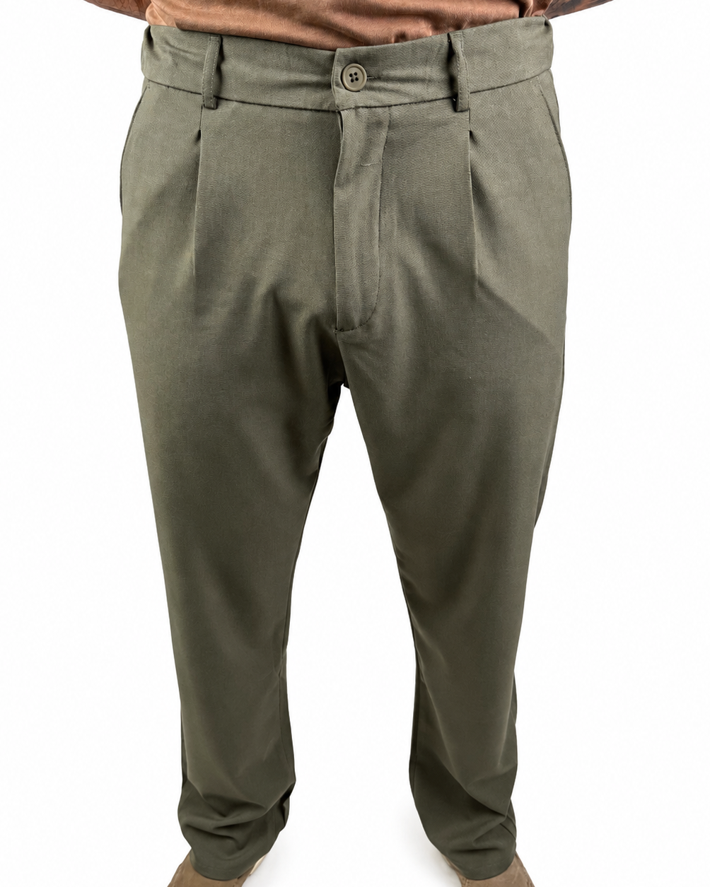 A person wearing olive green dress pants with a button closure and belt loops, paired with a brown shirt and brown shoes, shown from the waist down on a white background.