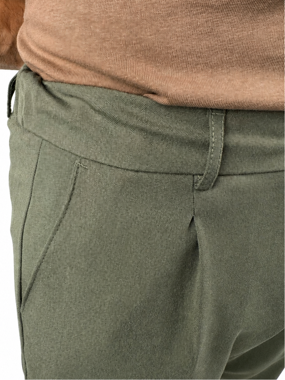 Close-up of a person wearing olive green trousers and a brown knit top against a white background.