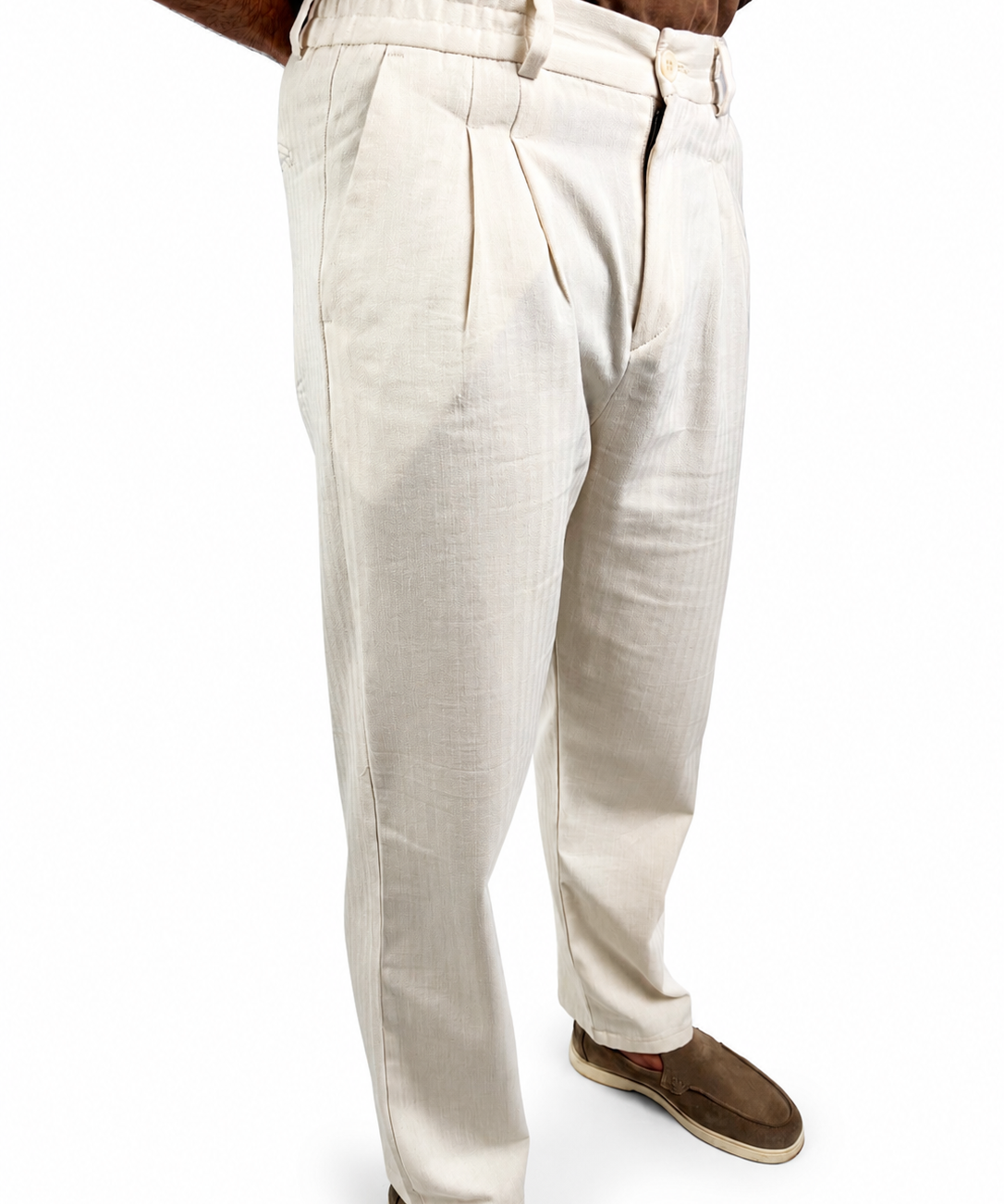 A person wearing off-white pleated trousers and brown slip-on shoes, shown from the waist down against a plain white background.