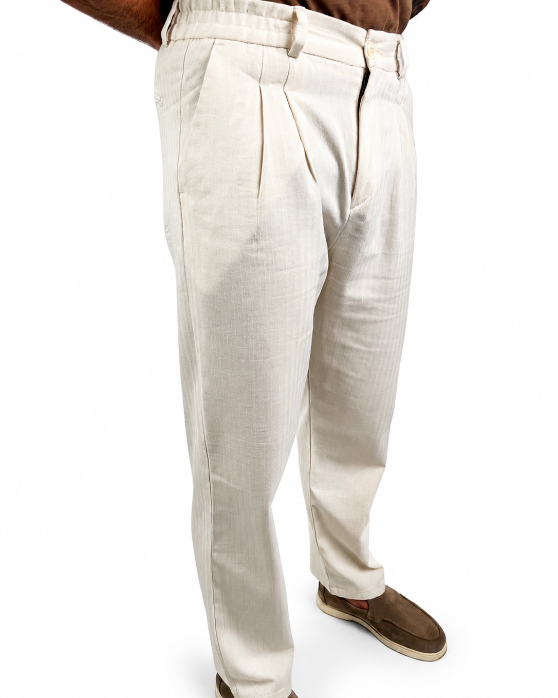 A person wearing off-white pleated trousers and brown slip-on shoes, shown from the waist down against a plain white background.