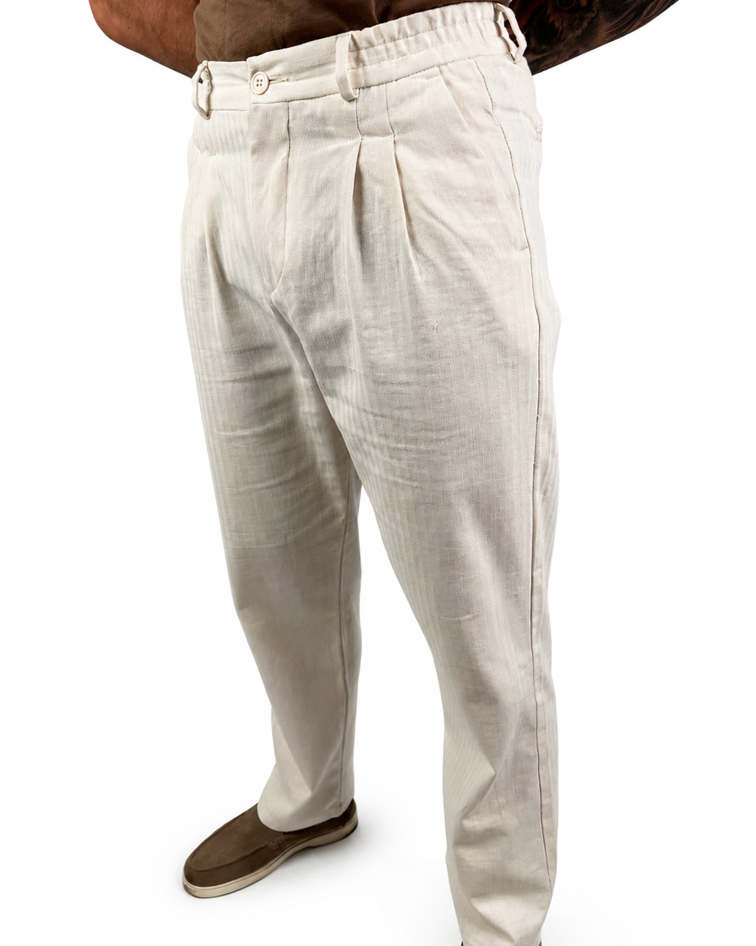 A person wearing off-white pleated linen trousers and brown slip-on shoes, shown from the waist down against a plain white background.