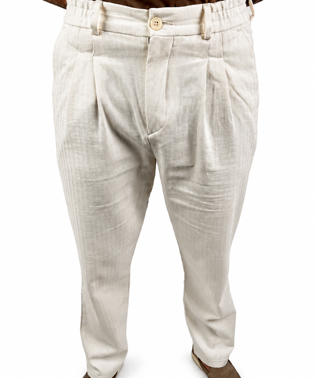 A person wearing light beige pleated trousers with a textured linen-like fabric, paired with brown shoes against a plain white background.