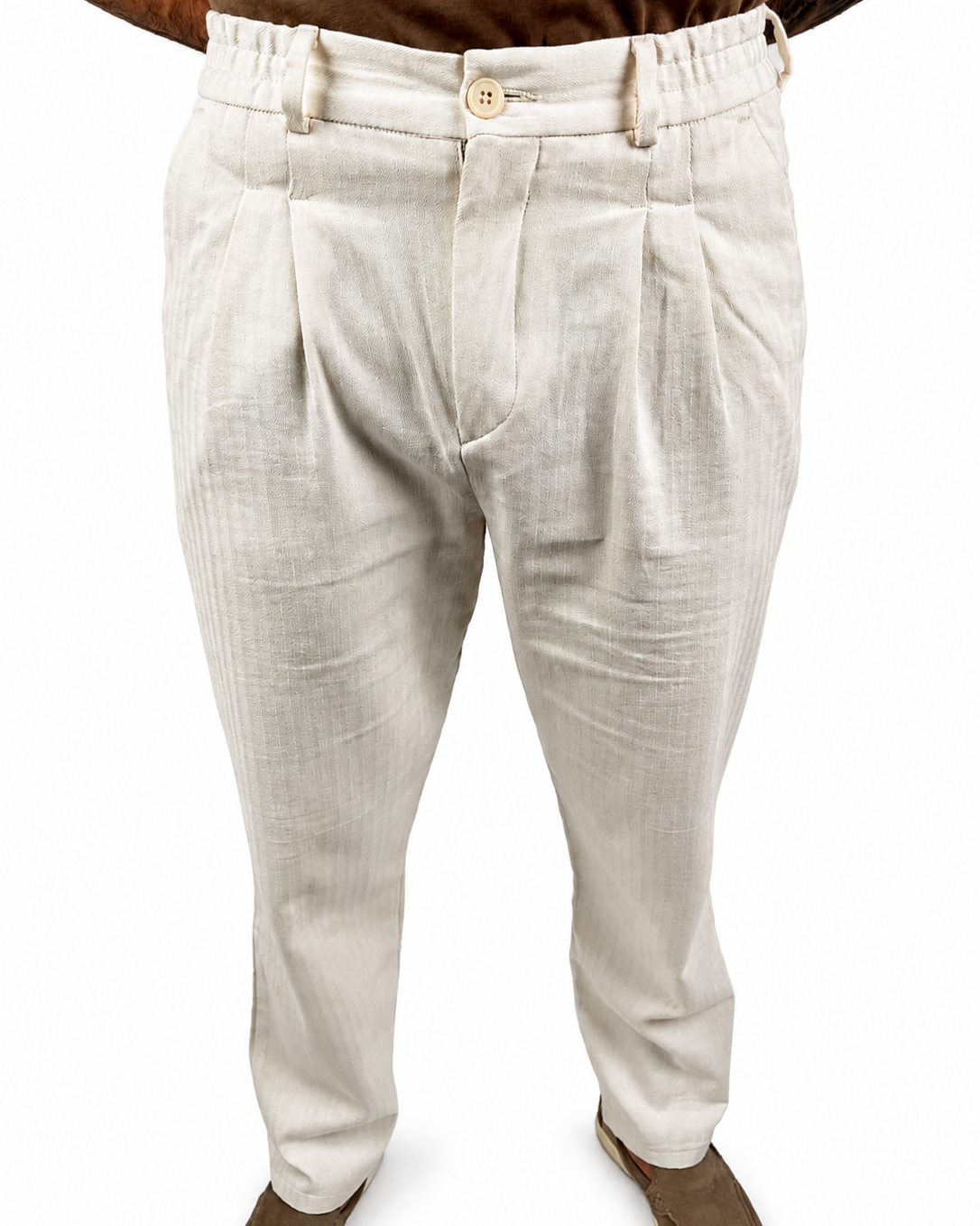 A person wearing light beige pleated trousers with a textured linen-like fabric, paired with brown shoes against a plain white background.