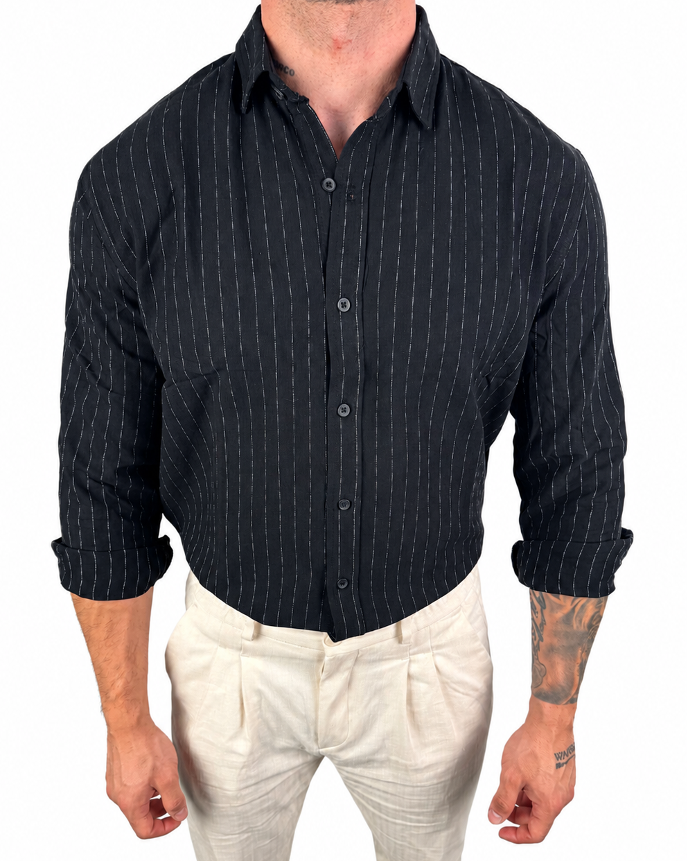 A man wearing a black long-sleeve button-down shirt with thin white vertical pinstripes and light beige trousers, shown from the neck down against a plain white background.