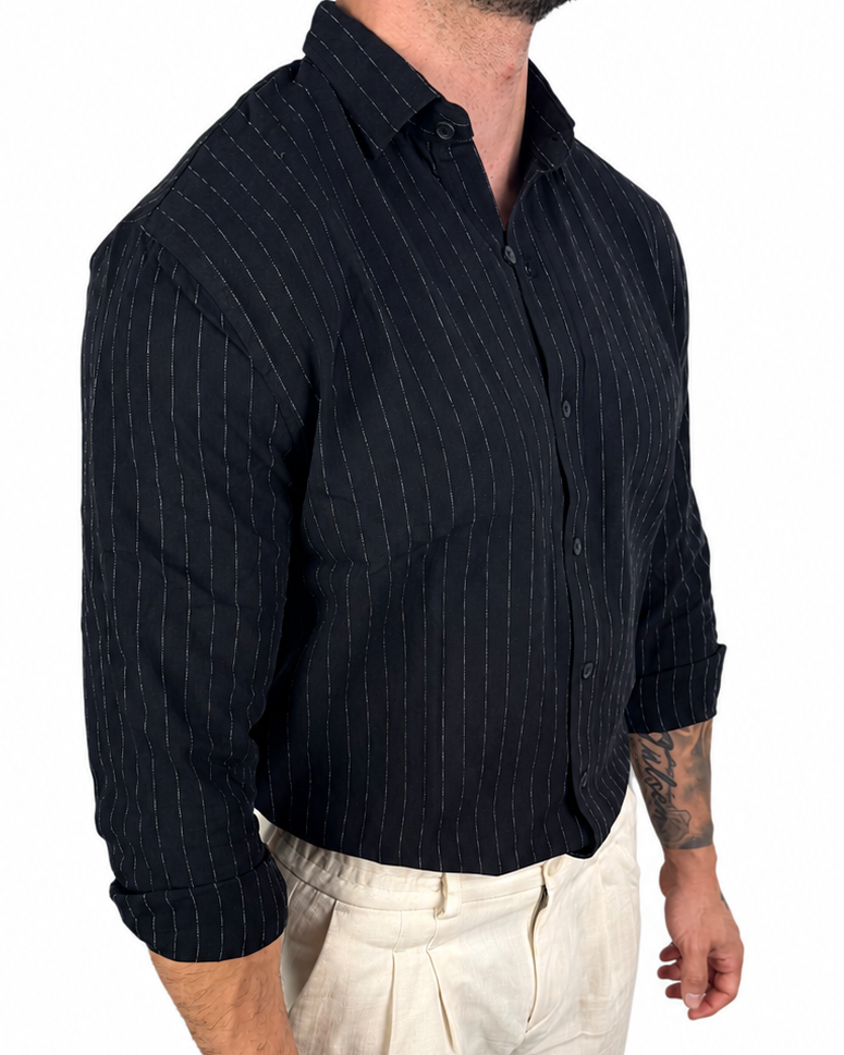 A man wearing a dark navy blue long-sleeve button-down shirt with thin vertical white pinstripes, paired with light beige trousers, shown from the waist down against a plain white background.