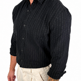 A man wearing a black long-sleeve button-up shirt with thin white vertical pinstripes and light beige trousers, shown from the waist up against a plain white background.