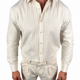 A man wearing a cream-colored linen button-down shirt with thin vertical blue stripes and matching linen trousers, shown from the neck down against a white background.