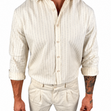 A man wearing a cream-colored linen shirt and matching trousers with thin vertical stripes, shown from the neck down against a plain white background.