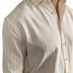 A man wearing a light beige cotton shirt with thin vertical dark pinstripes, shown from the chest down against a plain white background.