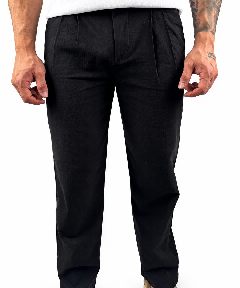 A man wearing black trousers and a white t-shirt, shown from the waist down against a plain white background.
