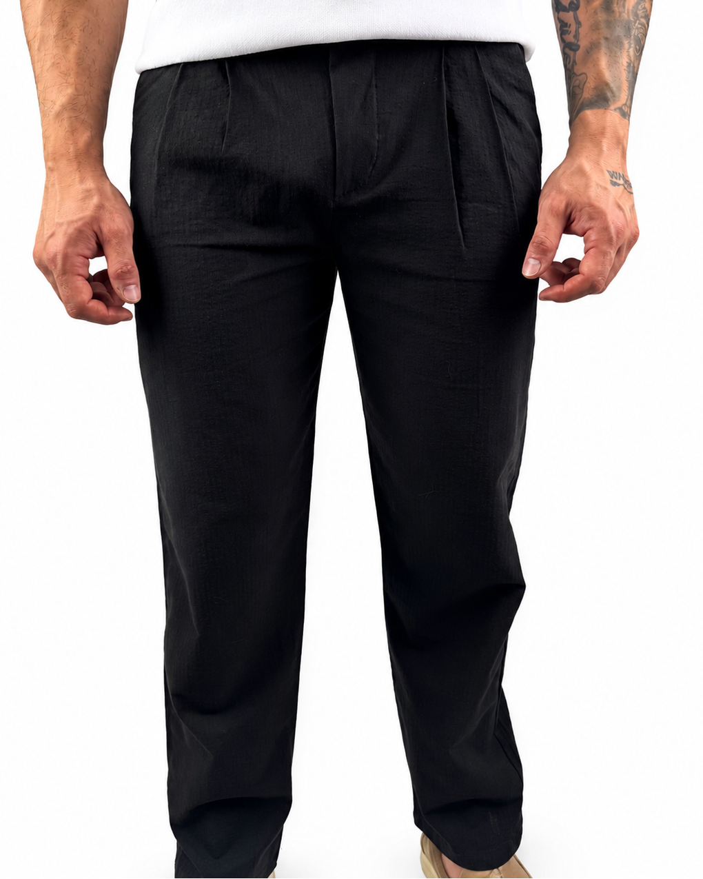 A man wearing black trousers and a white t-shirt, shown from the waist down against a plain white background.